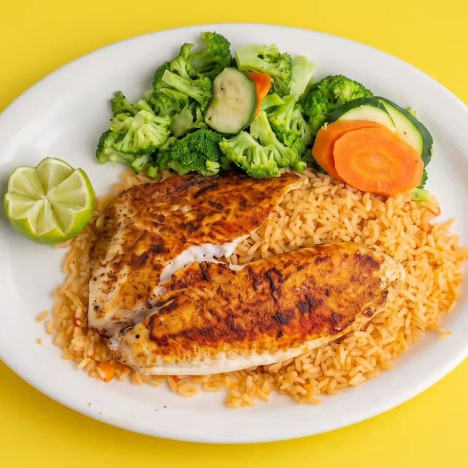 Two seasoned grilled fish fillets served over rice with broccoli, zucchini, carrot, and lime on a white plate.